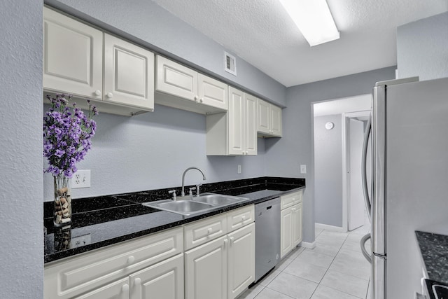 kitchen with a textured ceiling, light tile patterned flooring, sink, appliances with stainless steel finishes, and white cabinets