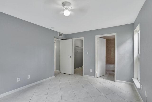 unfurnished bedroom featuring light tile patterned floors, ensuite bath, a closet, a spacious closet, and ceiling fan