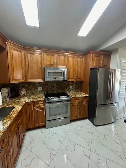 kitchen with light stone countertops, appliances with stainless steel finishes, backsplash, and sink