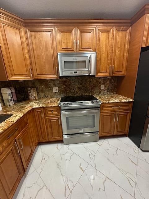 kitchen with decorative backsplash, stainless steel appliances, and light stone counters