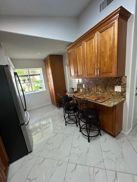 kitchen with refrigerator, tasteful backsplash, a textured ceiling, dark stone countertops, and lofted ceiling