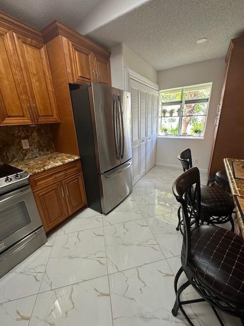 kitchen with backsplash, light stone counters, a textured ceiling, and appliances with stainless steel finishes