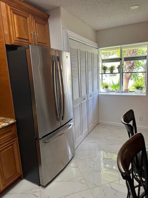 kitchen with light stone countertops, stainless steel fridge, and a textured ceiling