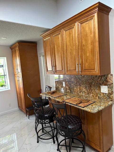 interior space featuring stone counters, a textured ceiling, a breakfast bar, and tasteful backsplash