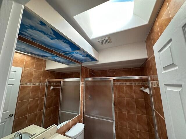 bathroom featuring vanity, toilet, an enclosed shower, and tile walls