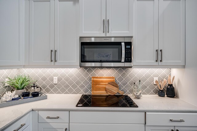 kitchen featuring white cabinetry, backsplash, black electric stovetop, and light stone countertops