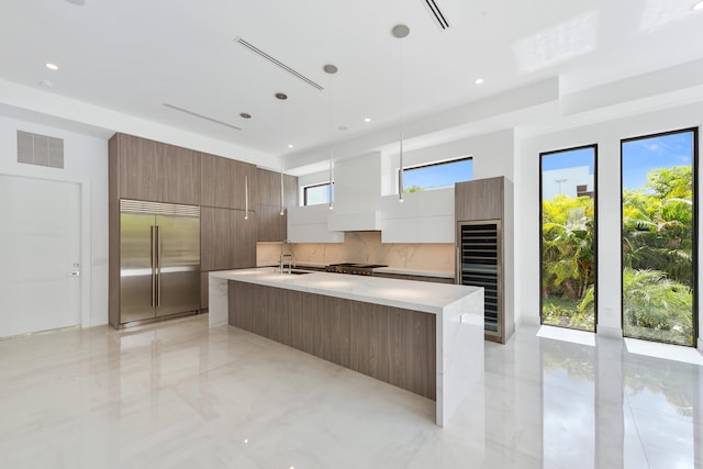 kitchen with a kitchen island with sink, decorative light fixtures, stainless steel appliances, and backsplash