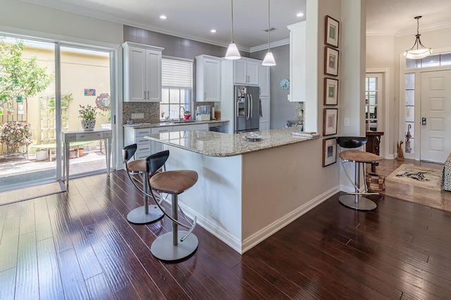 kitchen with decorative light fixtures, a kitchen bar, white cabinetry, and stainless steel fridge