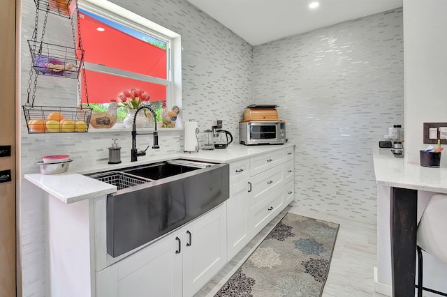 kitchen featuring white cabinets, tasteful backsplash, sink, and light stone countertops