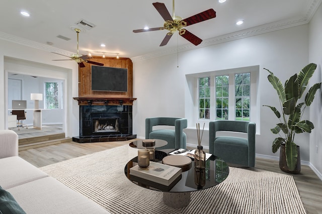 living room featuring ceiling fan, a tile fireplace, hardwood / wood-style flooring, and crown molding