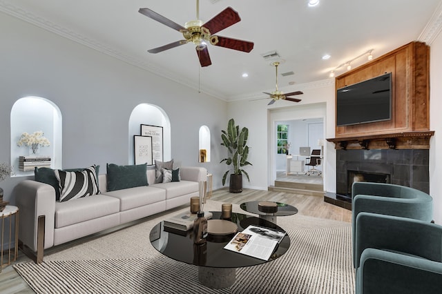 living room featuring ceiling fan, a tiled fireplace, light hardwood / wood-style floors, and ornamental molding