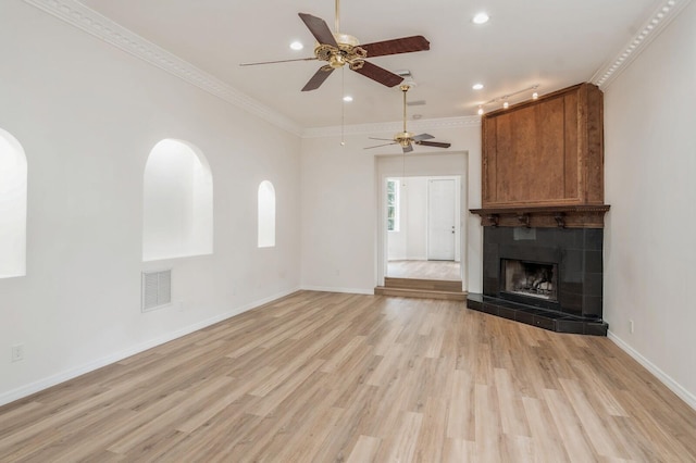 unfurnished living room with ornamental molding, light hardwood / wood-style flooring, ceiling fan, and a tiled fireplace