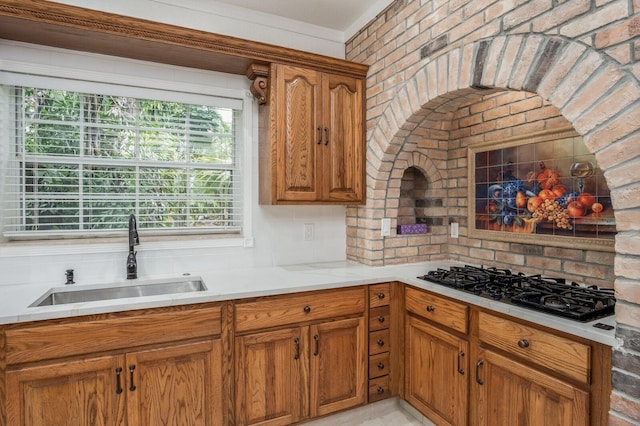 kitchen with brick wall, black gas stovetop, backsplash, ornamental molding, and sink