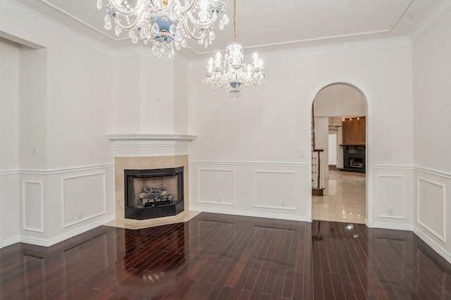 unfurnished living room with crown molding, dark hardwood / wood-style flooring, a tiled fireplace, and an inviting chandelier