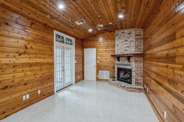 unfurnished living room with a fireplace, wooden walls, ceiling fan, french doors, and lofted ceiling