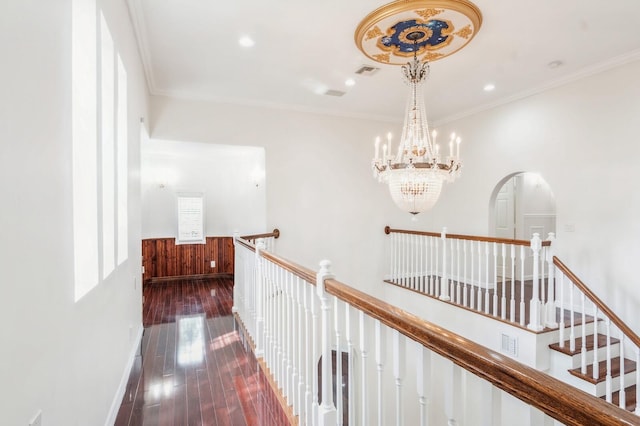 hallway featuring crown molding, dark wood-type flooring, a chandelier, and wooden walls