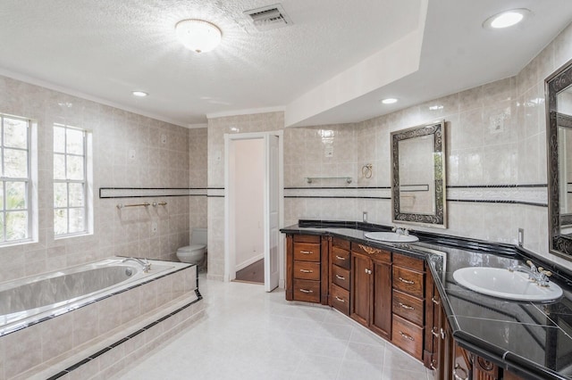 bathroom featuring tiled tub, toilet, tile patterned flooring, vanity, and tile walls