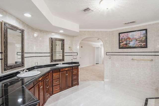 bathroom featuring a textured ceiling, vanity, tile walls, and tile patterned flooring