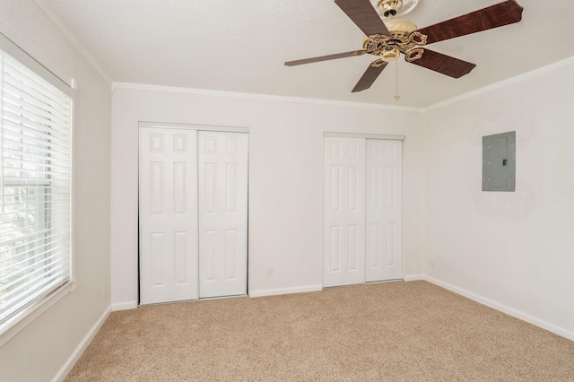 unfurnished bedroom with ornamental molding, two closets, electric panel, carpet flooring, and ceiling fan