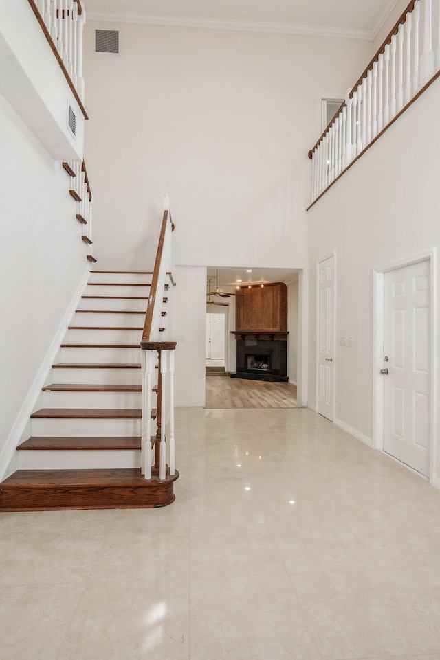 stairs with tile patterned flooring, crown molding, and a high ceiling