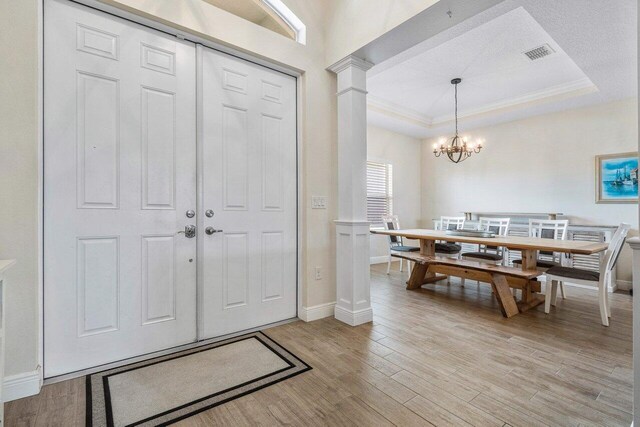 entryway with a notable chandelier, light wood-type flooring, and a tray ceiling