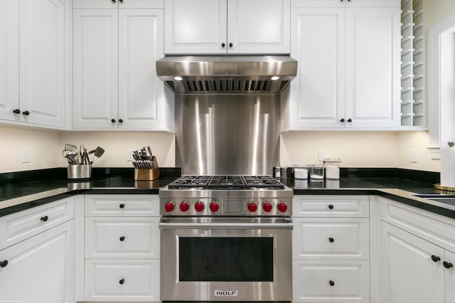 kitchen with wall chimney exhaust hood, white cabinets, and designer stove