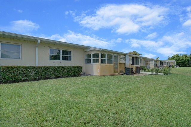 rear view of house featuring central air condition unit and a lawn