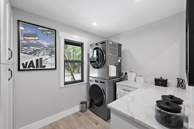 clothes washing area featuring stacked washing maching and dryer, cabinets, and light wood-type flooring