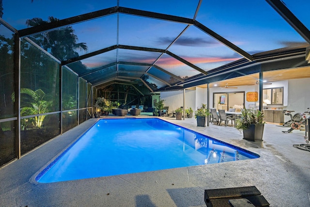 pool at dusk with ceiling fan, a lanai, and a patio area