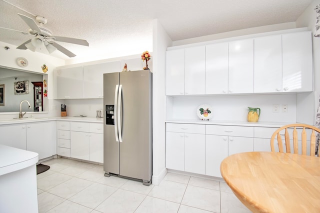 kitchen with light tile patterned floors, ceiling fan, sink, white cabinetry, and stainless steel fridge