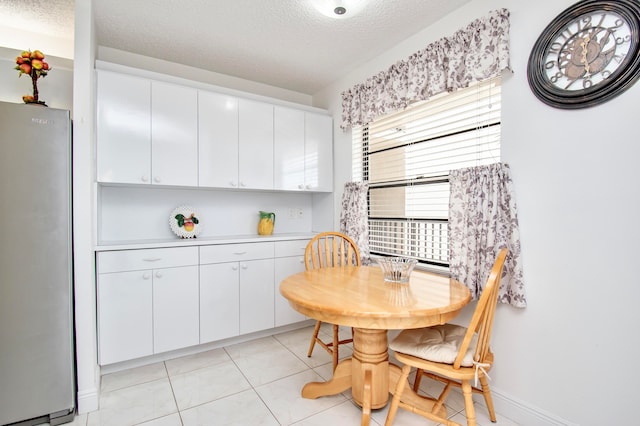 kitchen with white refrigerator, white cabinetry, a wealth of natural light, and light tile patterned floors