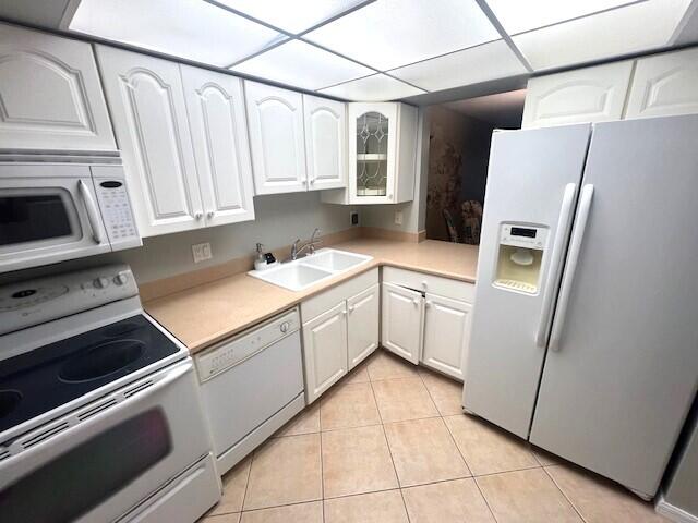 kitchen featuring light tile patterned flooring, white appliances, sink, and white cabinetry