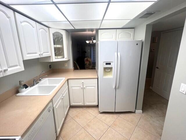 kitchen with white appliances, a notable chandelier, white cabinetry, light tile patterned floors, and sink