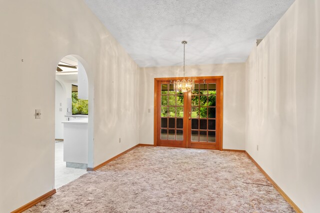 carpeted spare room with a textured ceiling and a chandelier