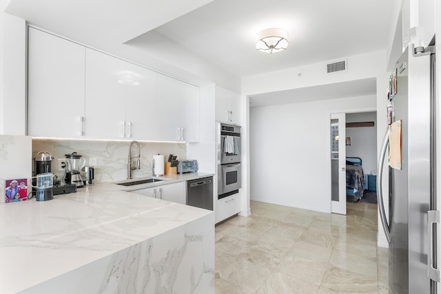 kitchen featuring white cabinetry, tasteful backsplash, sink, light stone countertops, and appliances with stainless steel finishes