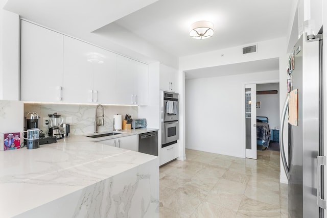 kitchen featuring a sink, white cabinetry, appliances with stainless steel finishes, backsplash, and light stone countertops