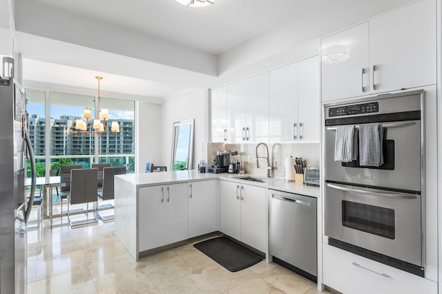 kitchen with backsplash, stainless steel appliances, a chandelier, white cabinetry, and kitchen peninsula