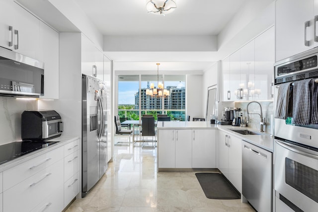 kitchen featuring pendant lighting, white cabinetry, a chandelier, stainless steel appliances, and sink