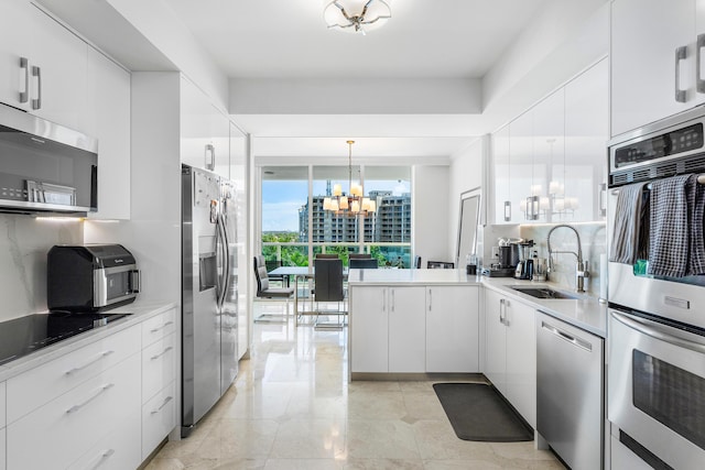 kitchen featuring a notable chandelier, a sink, white cabinetry, appliances with stainless steel finishes, and backsplash