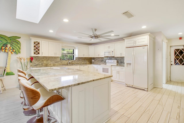 kitchen featuring backsplash, a kitchen bar, light stone counters, white appliances, and ceiling fan