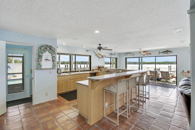 kitchen with a breakfast bar, light brown cabinetry, ceiling fan, a kitchen island, and light tile patterned floors