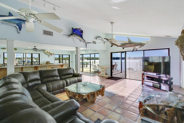 tiled living room with ceiling fan, a textured ceiling, lofted ceiling, and track lighting