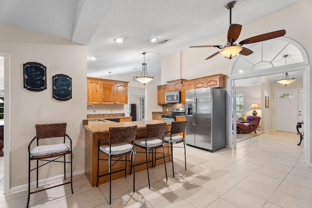 kitchen featuring lofted ceiling, sink, a breakfast bar area, light stone counters, and stainless steel appliances