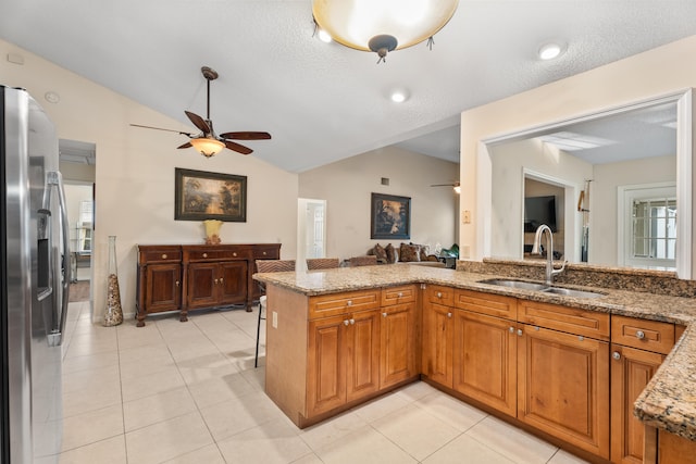 kitchen featuring stainless steel refrigerator with ice dispenser, ceiling fan, sink, light tile patterned flooring, and light stone counters