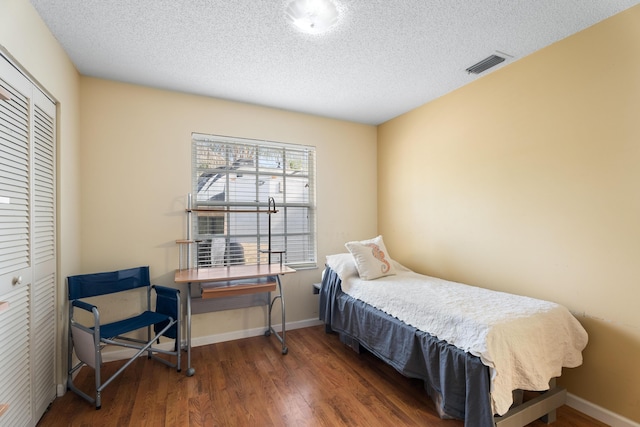 bedroom with a textured ceiling, dark hardwood / wood-style flooring, and a closet