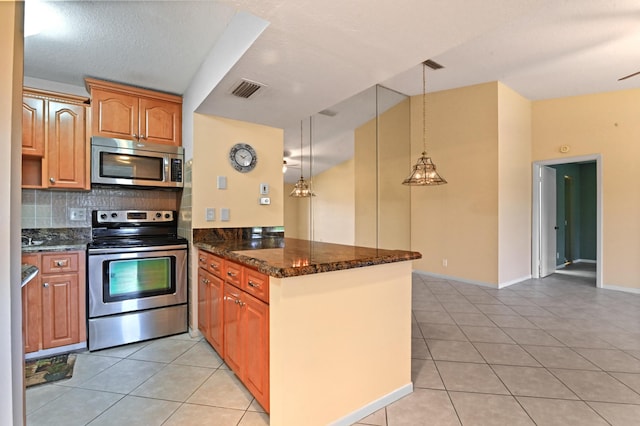 kitchen with light tile patterned flooring, dark stone countertops, appliances with stainless steel finishes, kitchen peninsula, and pendant lighting