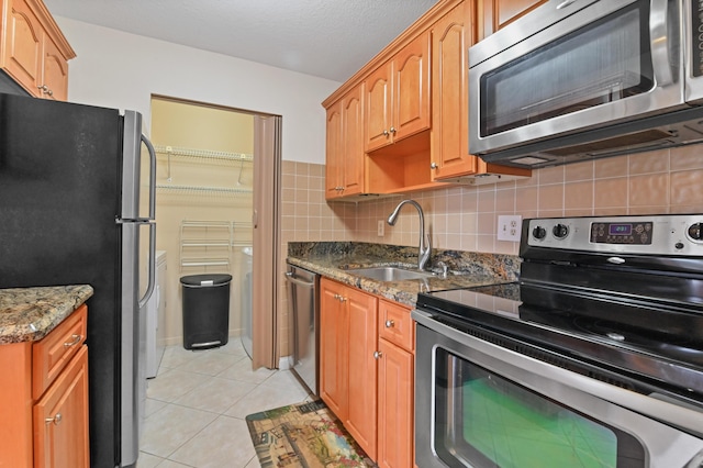 kitchen featuring light tile patterned flooring, sink, dark stone countertops, appliances with stainless steel finishes, and decorative backsplash