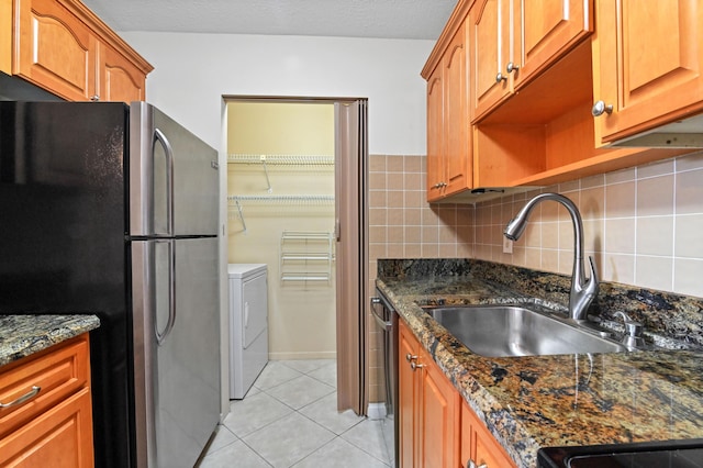 kitchen featuring appliances with stainless steel finishes, washer and clothes dryer, sink, and dark stone countertops