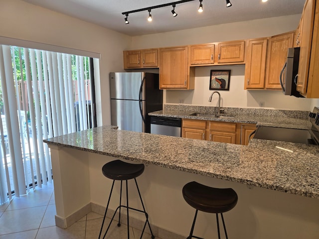 kitchen featuring stainless steel appliances, a kitchen bar, track lighting, sink, and stone counters