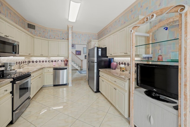 kitchen with cream cabinets, tasteful backsplash, sink, stainless steel appliances, and light tile patterned floors